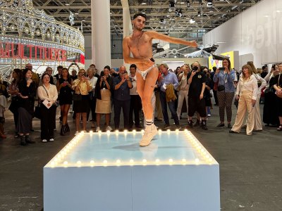 A go-go boy in silver lamé speedo dances on a blue-painted platform.