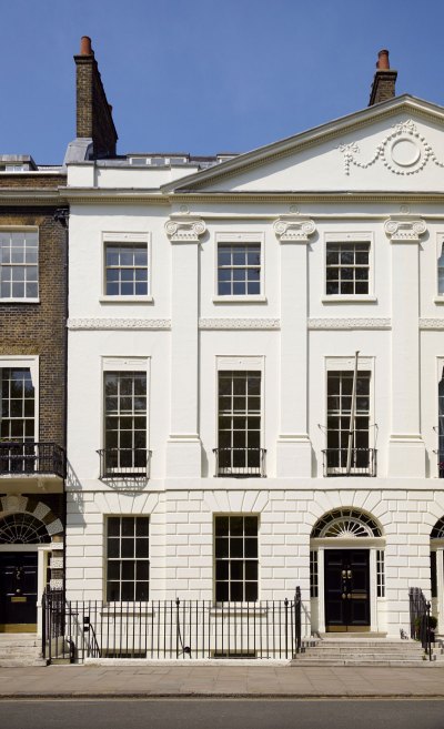 View of the exterior of a tony British townhouse that has a white facade. 