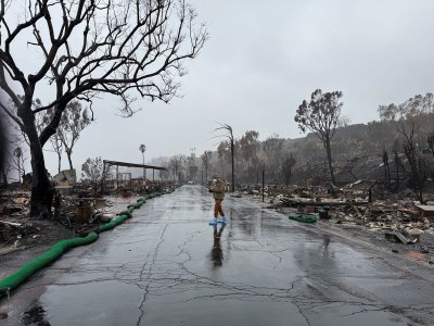 A person walks through a neighborhood that has been completely burned down on a rainy, overcast day. 