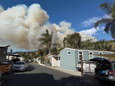 A residential street on a sunny with the smoke of an approaching wildfire visible in the center background. 