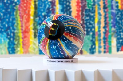 A Magic Eight with an abstract design sits on a pedestal in front of the abstract artwork that inspired it.