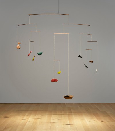 A sculpture resembling a mobile with ship- and animal-like abstract elements that dangle above a wood floor.