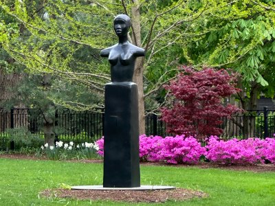 A bronze bust on a tall plinth installed in a lush garden.