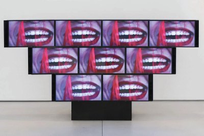 A sculptural video installation of an inverse pyramid, showing a close-up of a laughing mouth.