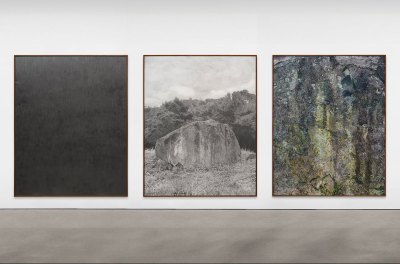 Three large drawings hang on a all. From left an all-black graphite surface, a gray drawing of a rock in a landscape, an abstract painting that is perhaps a close-up of a mossy rock.