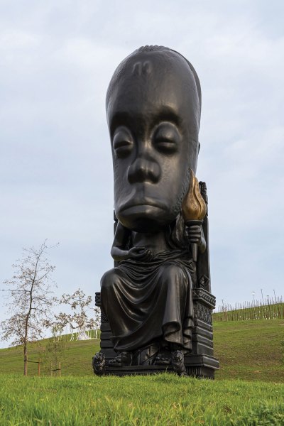 A large-scale sculpture in a vineyard. Its head resembles an African mask.
