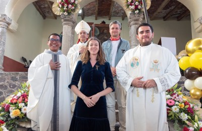 Three clergy members and two lay people pose for a photo with a painting in the background. 