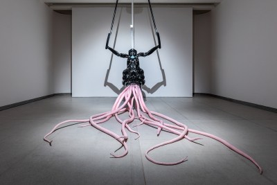 A sculpture of a black humanoid creature with long pink tentacles.