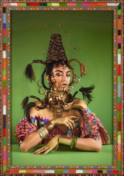A photograph of a person seated a green table with her hair braided to resemble a hive.