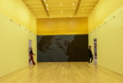Two people walking through an empty room with yellow lighting and a hanging net.