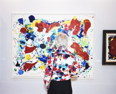 A woman in a shirt with black, red, and purple splotches that resembles an abstract painting she is looking at.
