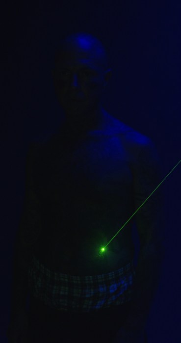 A person in a dark blue space with a green laser aimed at their stomach.