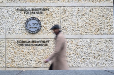 A person walking by a building with signs for the National Endowment for the Arts and the National Endowment for the Humanities.