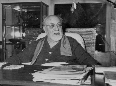 Portrait of Henri Matisse at a desk with books on it.