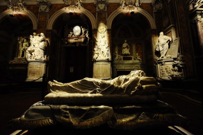 A dramatically lit sculpture of a veiled figure on a bed surrounded by other marble sculptures.