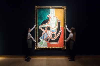 Two people holding up an abstract painting.
