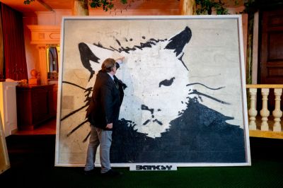 A man stands in front of a painting of a rat.