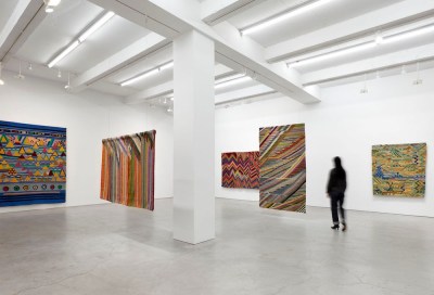 A person walking through an exhibition of freestanding abstract weavings.