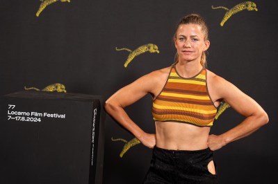 A white woman in a striped orange and yellow top standing with her hands at her waist next to a podium.