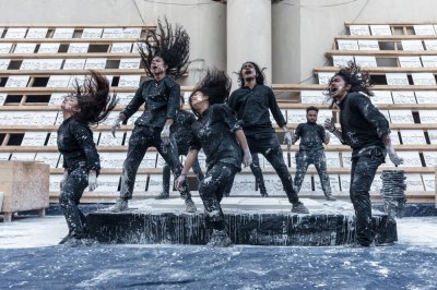 A group of people wearing all black and sprayed with white paint jump up and down dramatically.