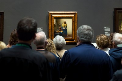 A crowd of people looking at painting of a woman pouring milk from a jug.
