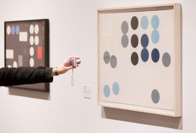 A person pointing a camera at an abstract painting.