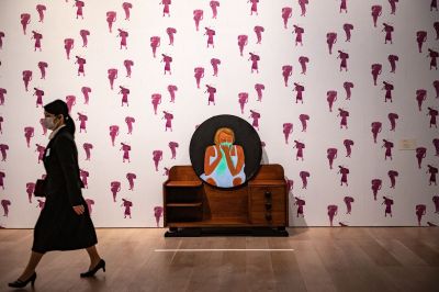 A woman walking past a dresser with a circular painting of a crying woman on it.