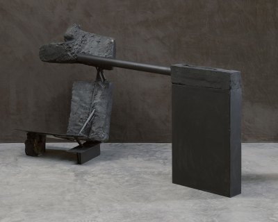 An installation of several black-painted elements, facing a black wall. 