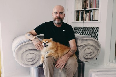 Portrait of Andreas Angelidakis seated in a chair resembling a column with a dog in his lap.